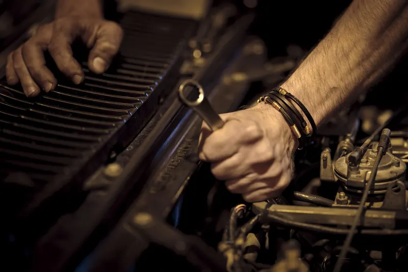 Greasy hands holding a wrench over a car engine.