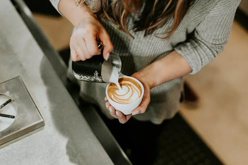 Hands pouring latte art into a white cup.