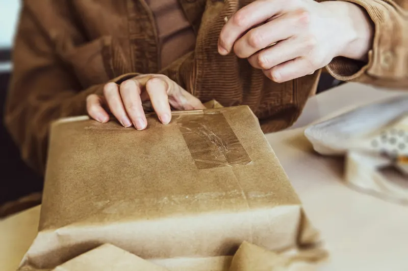 Hands taping up a parcel wrapped in brown paper.